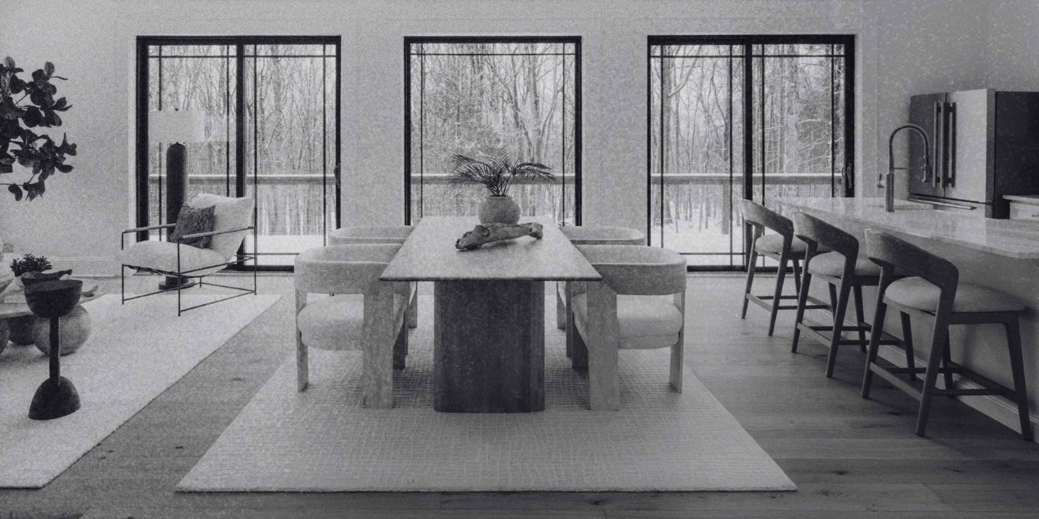 Dining area with a large table, kitchen island seating, floor-to-ceiling windows, and peaceful woodland views.