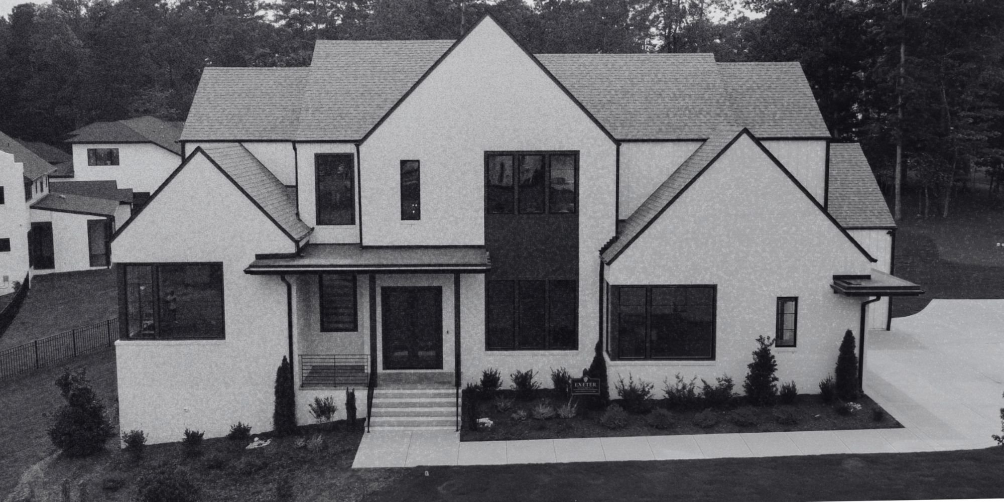 Contemporary custom home exterior featuring white siding, dark accents, large windows, and landscaped entry.
