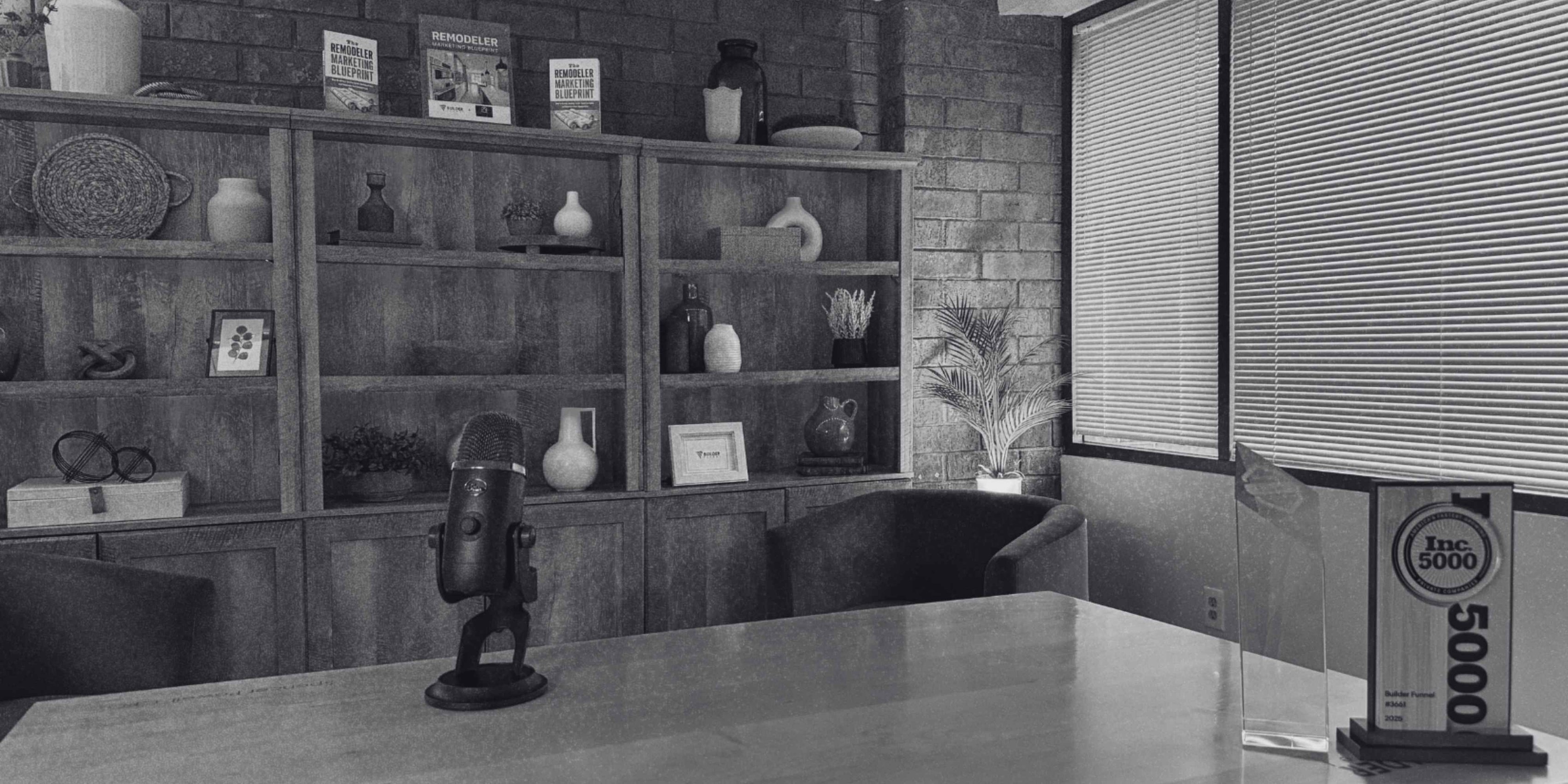 Podcast recording space with a tabletop microphone, built-in shelving, and an Inc. 5000 award.