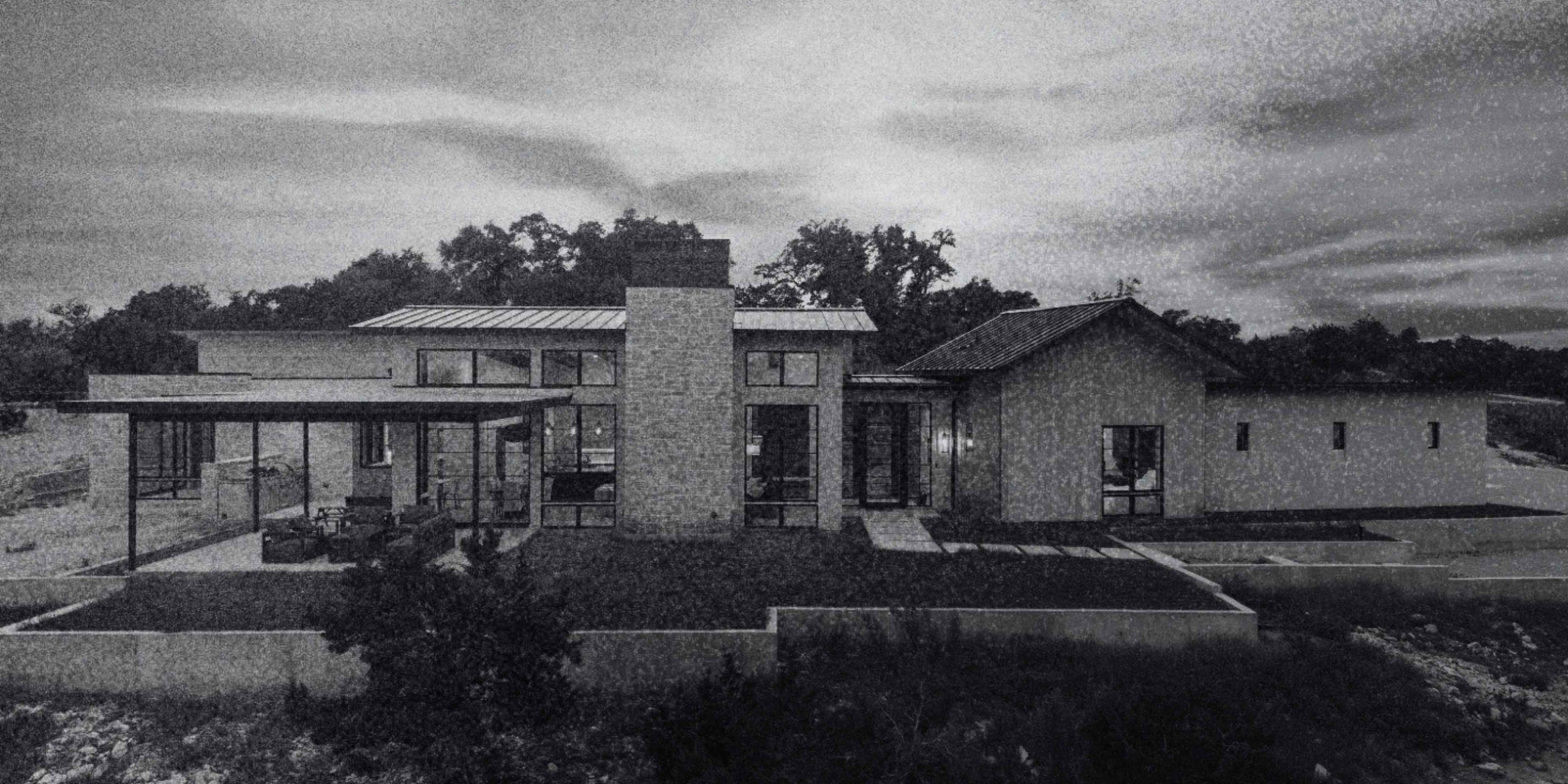 Custom home exterior featuring stonework, large windows, low rooflines, and an expansive covered patio.