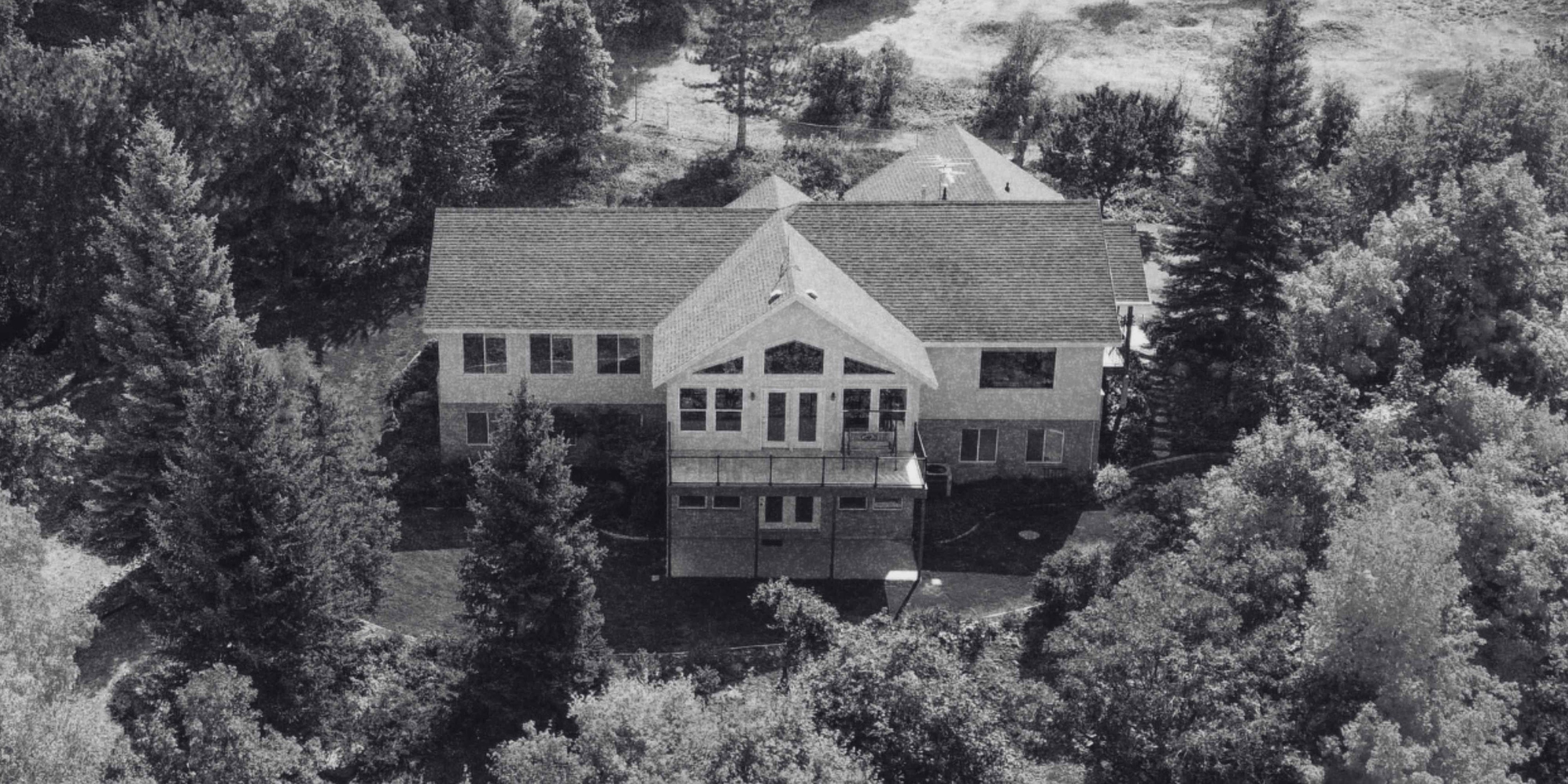 Aerial view of a custom home surrounded by mature trees with a large rear deck and expansive windows.