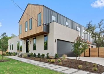 Contemporary two-story home with wood and metal siding, large windows, a dark garage door, and modern landscaping.