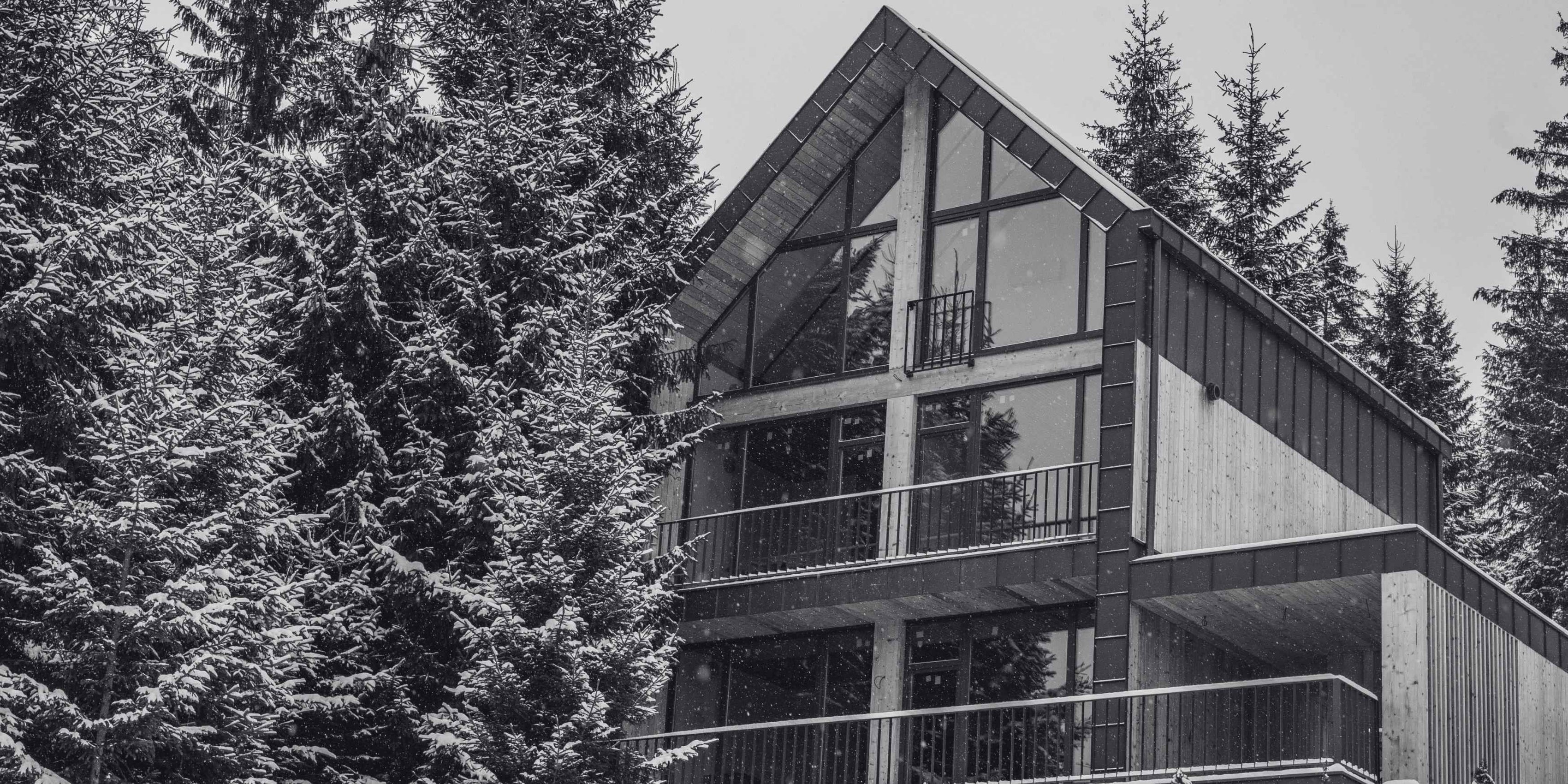 Mountain retreat surrounded by snow-covered evergreens with large windows, wood accents, and multiple balconies.
