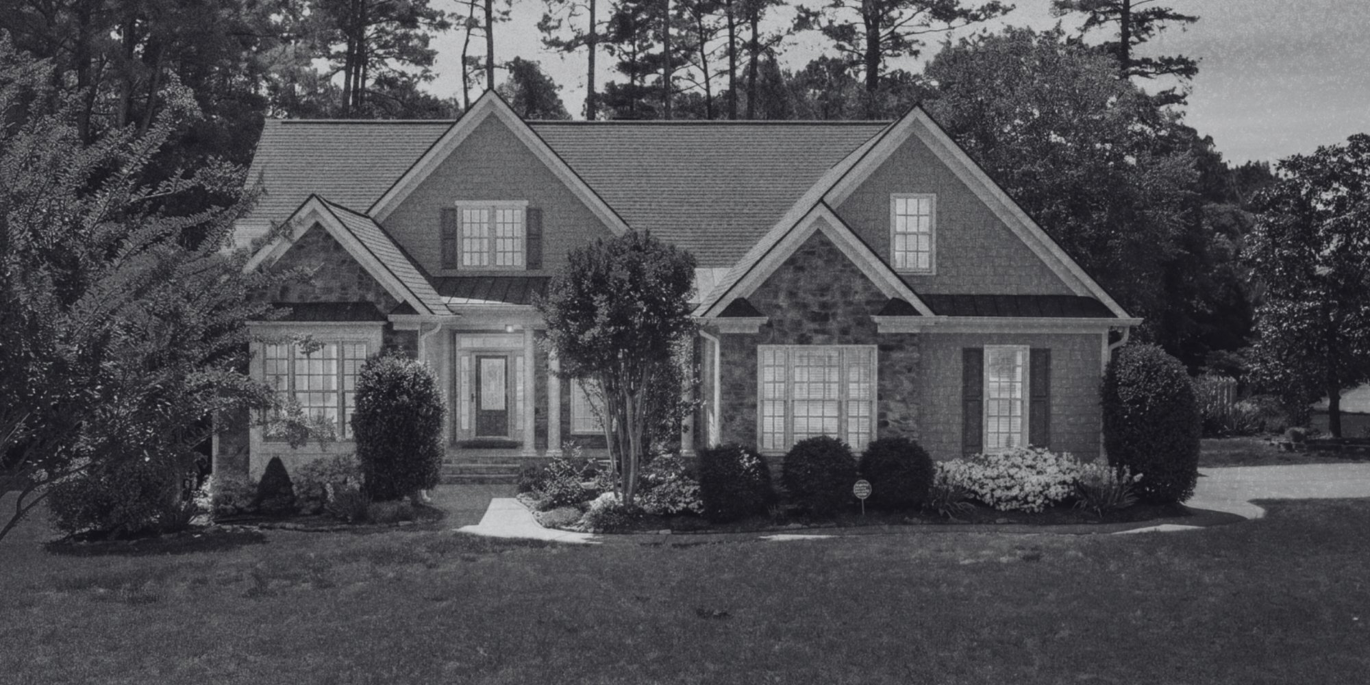 Traditional custom home exterior with stone accents, multiple gables, mature landscaping, and a covered entry.